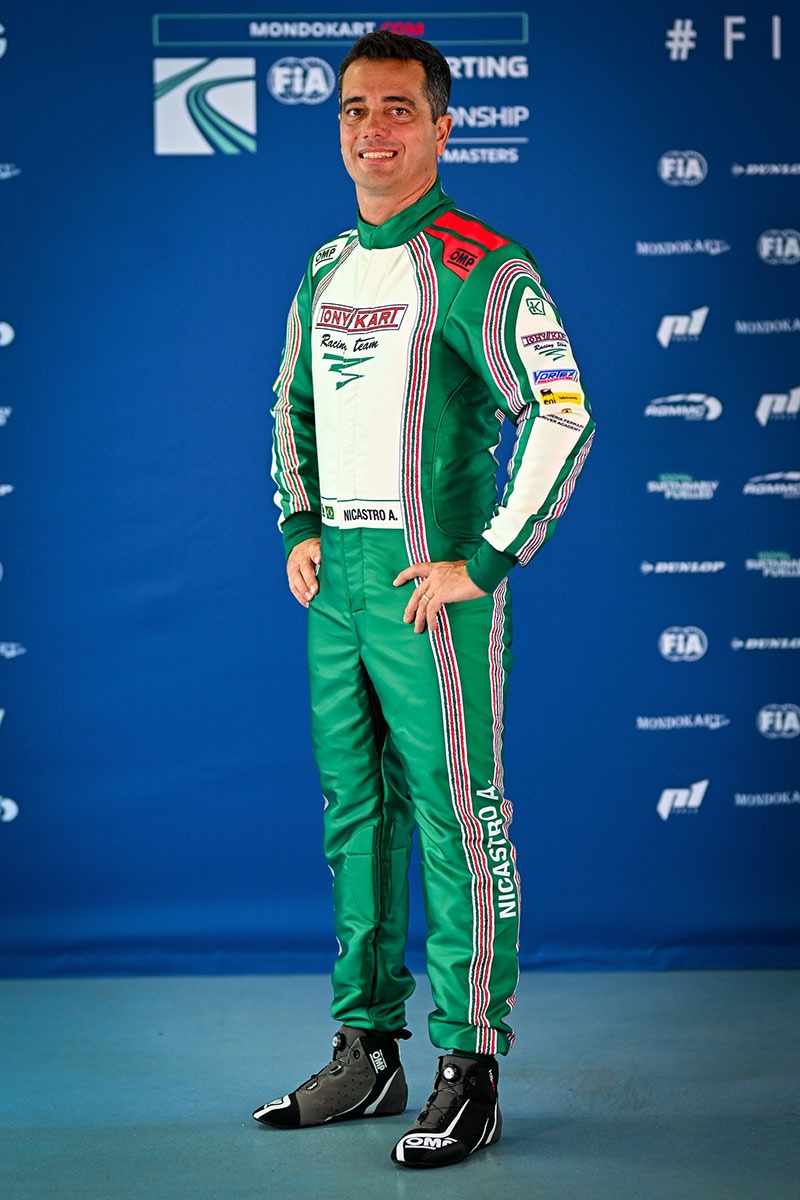 Tony Kart color scheme "Driver wearing a Tony Kart OMP racing suit in green, white, and red colors, posed in front of FIA Karting World Championship backdrop."