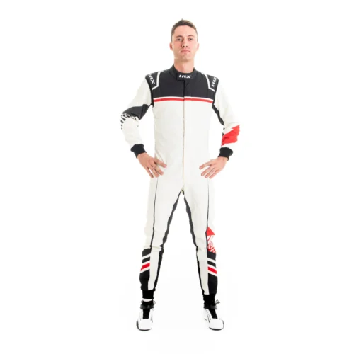 Male driver standing with hands on hips wearing a white HRX motorsport racing suit with black upper torso panels and sharp red line accents. Male driver standing with hands on hips wearing a white HRX motorsport racing suit with black upper torso panels and sharp red line accents.