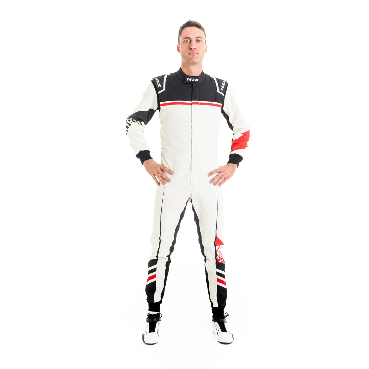 Male driver standing with hands on hips wearing a white HRX motorsport racing suit with black upper torso panels and sharp red line accents. Male driver standing with hands on hips wearing a white HRX motorsport racing suit with black upper torso panels and sharp red line accents.
