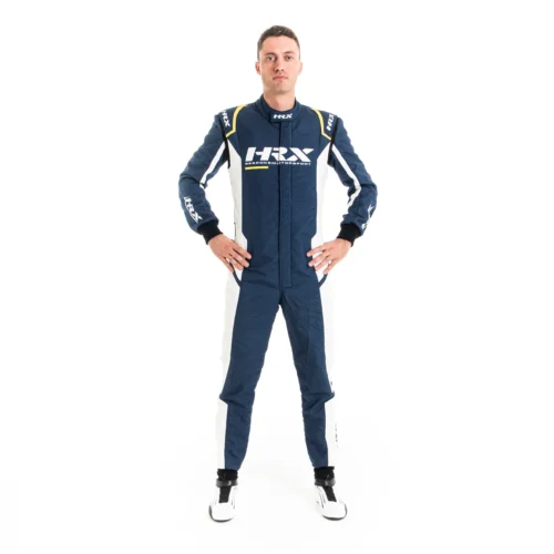 Male driver standing with hands on hips wearing a navy blue and white HRX motorsport racing suit with yellow shoulder trim accents.